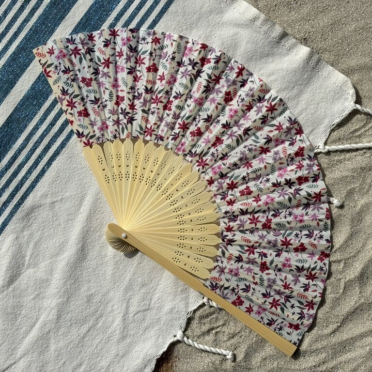 Éventail fleuri en tissu et bambou, idéal pour l’été Éventail original motifs fleurs violettes et roses en tissu et bambou posé sur serviette en extérieur