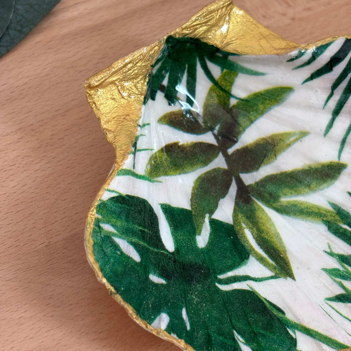 Détail finition dorée Détail du repose bijoux original coquillage feuillage tropical vert avec bordure dorée.