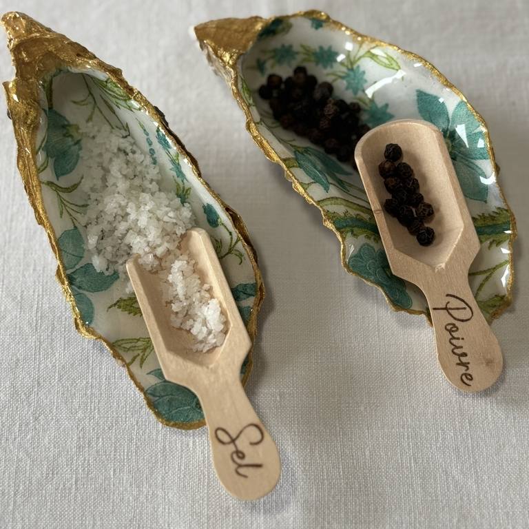 Mise en situation avec sel et poivre dans les coquilles motif fleurs bleues Gros plan sur les coquilles en forme naturelle décorées de fleurs bleues, dorées à la main, avec cuillères à sel et poivre.