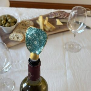 Bouchon de vin original motif géométrique bleu-vert sur bouteille de Bordeaux lors d’un apéritif.